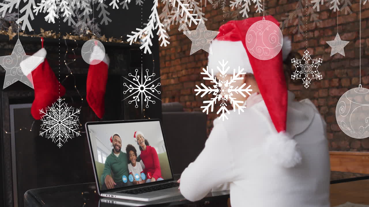 animación de nieve cayendo sobre una mujer sonriente en sombrero de santa en una llamada de video portátil con su familia