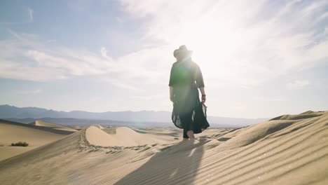 Silueta-De-Mujer-Vestida-Caminando-Descalza-En-Las-Dunas-De-Arena-Retroiluminada-Con-Sol-Brillante