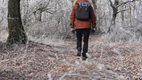 Caucasian-man-in-brown-winter-jacket-and-fluffy-hood-walking-into-frost-covered-forest