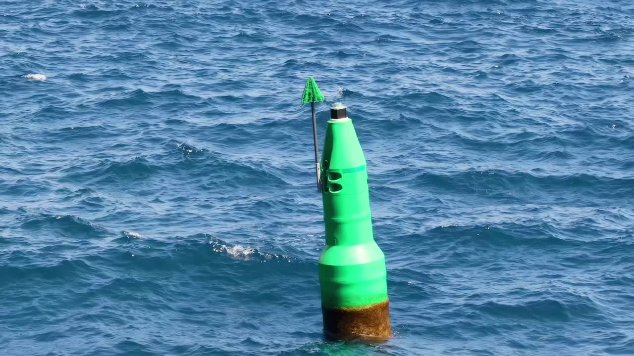 A solitary green buoy gently sways amidst the rhythmic ocean waves under a clear blue sky.