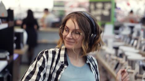 Retrato-De-Una-Linda-Mujer-Joven-Caucásica-Con-El-Pelo-Corto-Y-Rizado,-Camisa-A-Cuadros-Y-Auriculares-Bailando-Y-Escuchando-Música