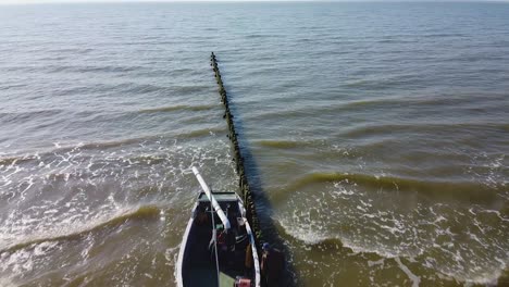 Beautiful-aerial-birdseye-view-of-green-coastal-fisherman-fishing-boat-docked-at-the-old-wooden-pier-in-sunny-day,-fisherman-checks-boat,-calm-sea-shore,-wide-angle-drone-shot-moving-forward