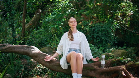 tranquil woman meditating greenery forest sitting trunk. girl breathing in park