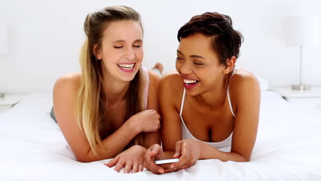 Two-pretty-friends-texting-on-smartphone-lying-on-bed