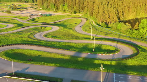 racers driving curved segments of a karting track under the evening sun