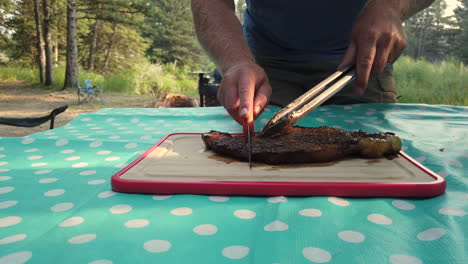 caucasian male cutting up grilled beef steak at campsite