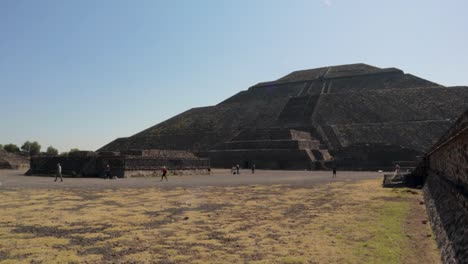 a wide dolly in slow motion shot of the pyramid of the sun at the teotihuacan archaeological site in mexico, with some tourists walking around and the blue sky on a clear and sunny day