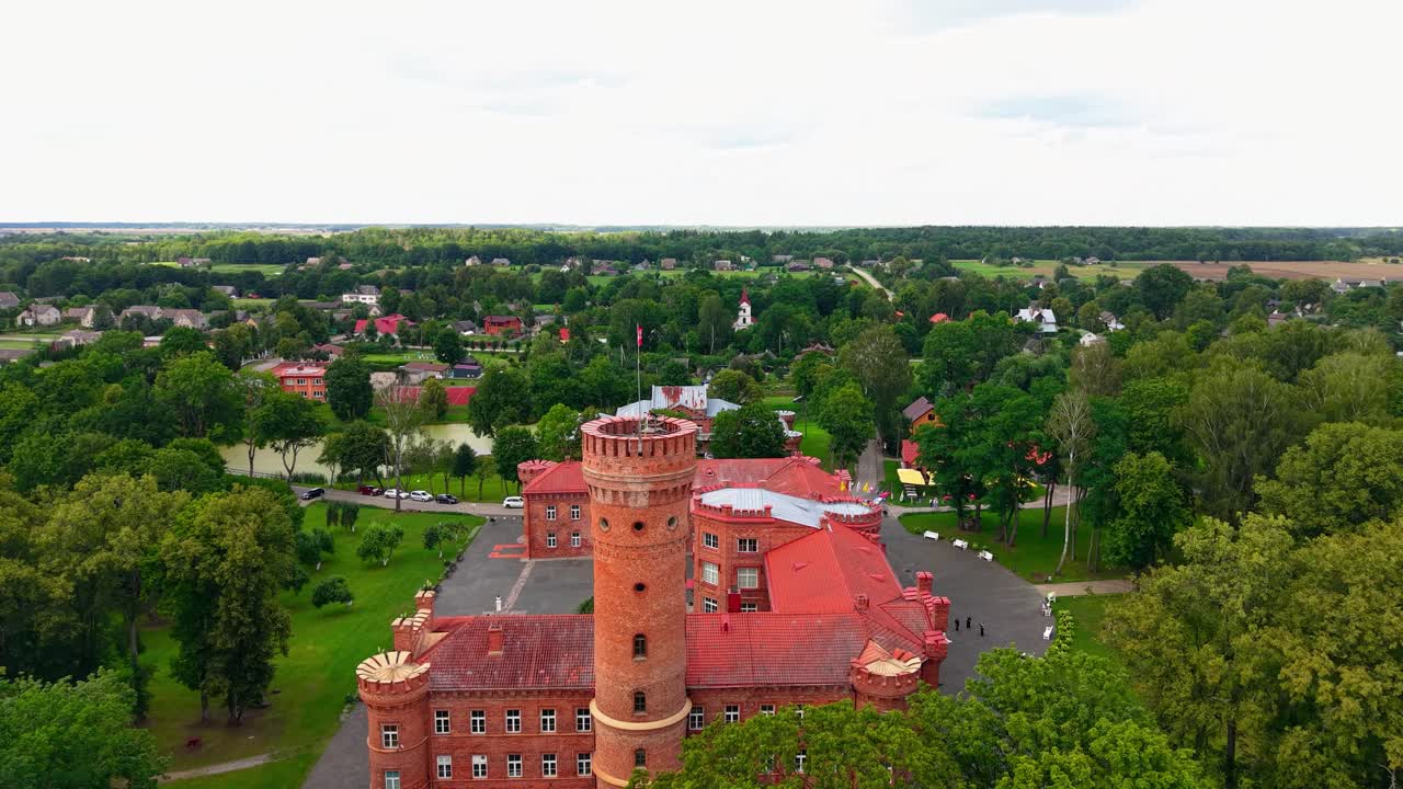 Aerial view of Raudonė Castle in Lithuania, a historic redbrick fortress surrounded by lush greenery and forest, showcasing beautiful architecture and peaceful countryside atmosphere
