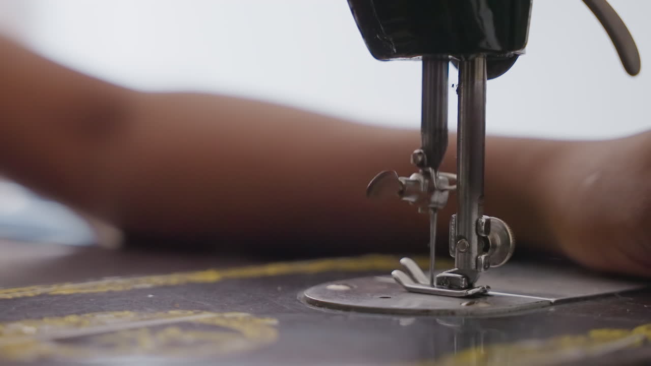 Primo piano di una macchina da cucire nera su un tavolo, il braccio di un lavoratore guida il tessuto sotto l'ago. Movimento costante del filo e del piedino, macchina in metallo vintage. Una scena di faccende domestiche con un'atmosfera intima.
