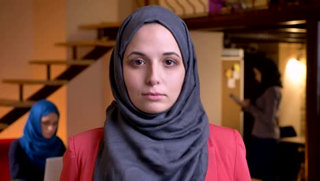 closeup portrait of young beautiful muslim businesswoman in gray hijab looking straight at camera being on the workplace indoors