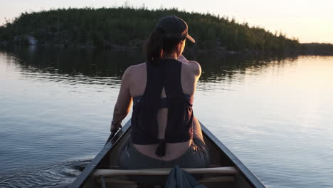 Millennial-women-paddling-a-canoe-at-sunset-with-green-wilderness-in-the-background