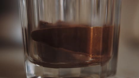 instant powdered coffee watered in transparent glass, shallow focus close-up, slowmo