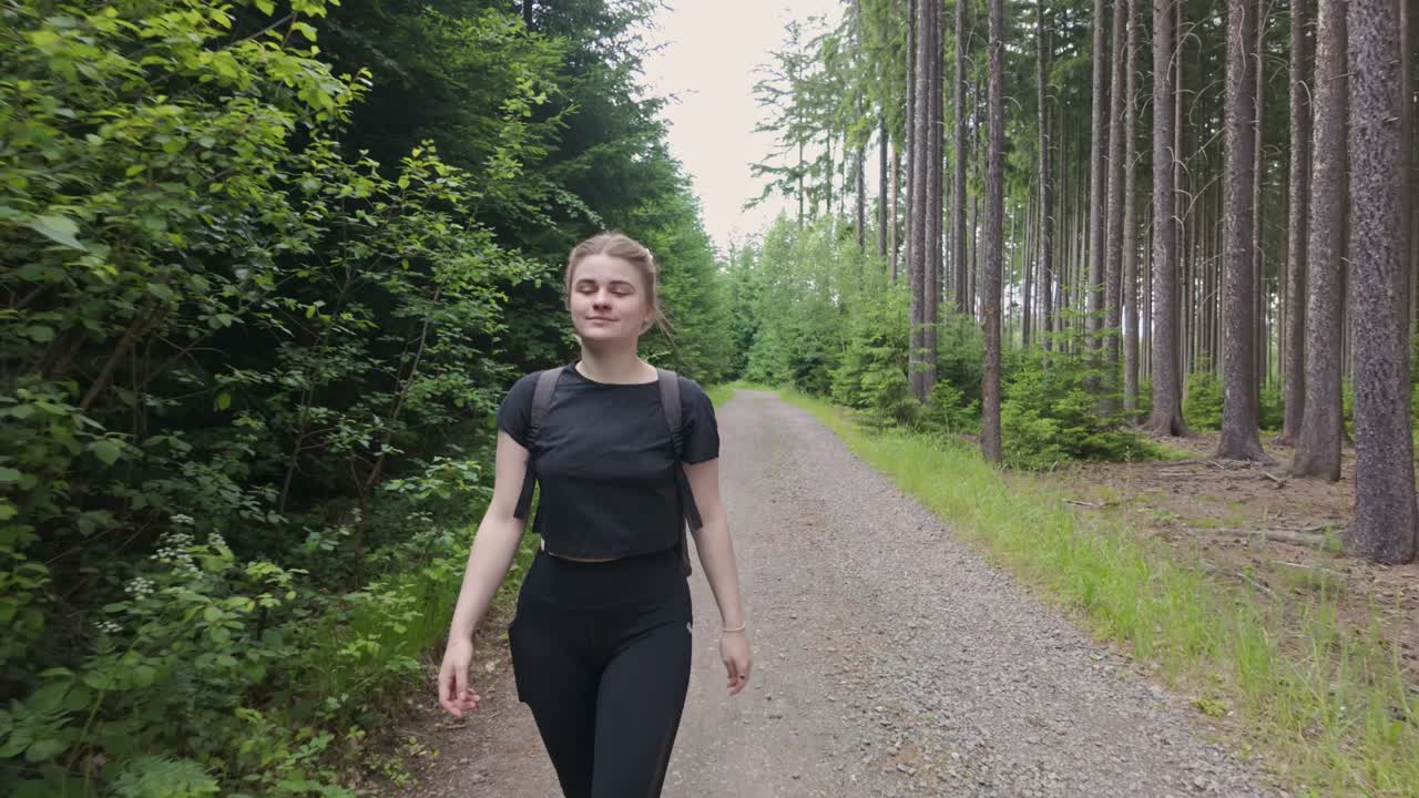 Entdecken Sie die heitere Schönheit der Natur, während ein fröhliches junges Mädchen eine ruhige Reise durch einen üppigen Waldweg unternimmt und sich an den Wundern des Reisens und Abenteuers erfreut.