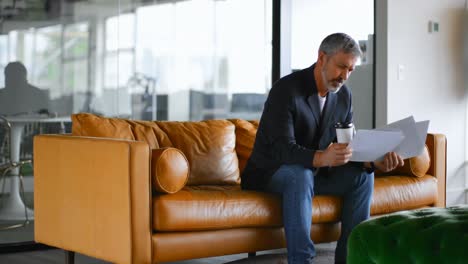 hombre de negocios con taza de café comprobando el documento en el sofá 4k
