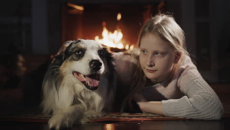 una niña abraza a su perro, tirado en el suelo cerca de la chimenea.