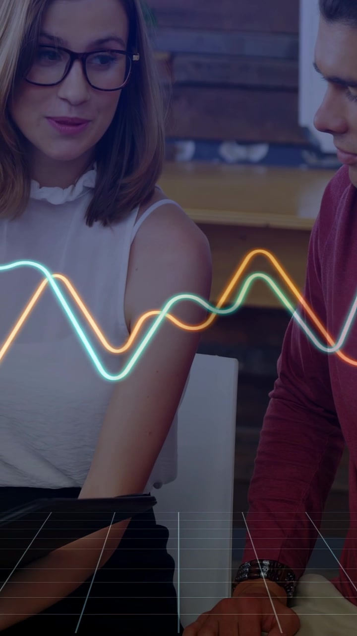 Video verticale: Donna che indica un dispositivo, esaminando dati con un collega uomo nel settore tecnologico, con onde che li avvolgono entrambi.