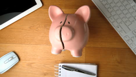 piggy bank falling on a desk beside tablet pc and keyboard