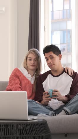 young couple on a video call with their laptop while sitting on a couch together at home.