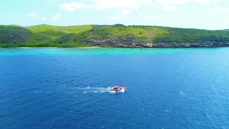 Drone-side-to-side-tracking-of-fishing-boat-slowly-moving-across-sea,-green-rocky-coastline