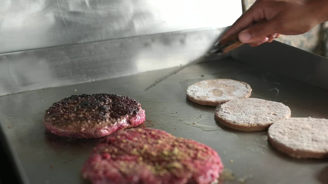 cocinero anónimo girando chuletas de hamburguesa calientes con espátula en la cocina