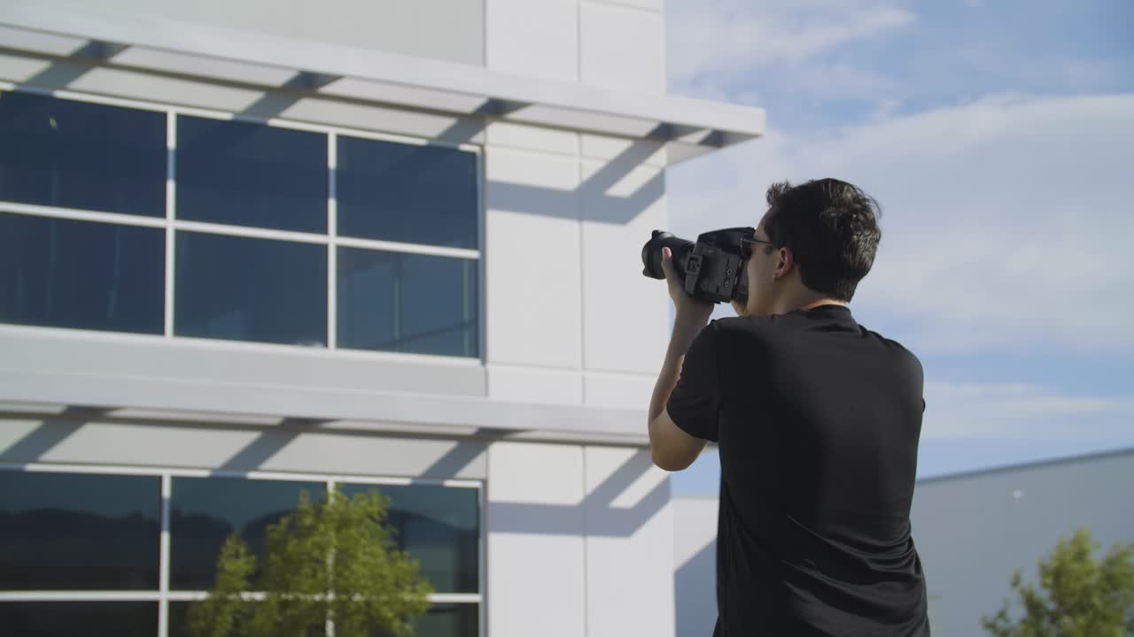 En fotograf tager eksteriørbilleder af en kontorbygning til en lokationsspejder på en blæsende dag
