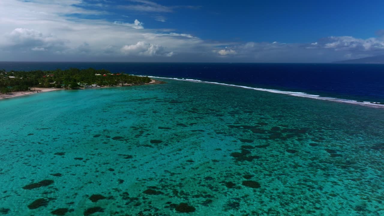 Luftfoto med drone af Moorea, Fransk Polynesien, med lavt koralrev, Opunohu-bugten og bølger i mørkeblåt vand ved Ta'ahiamanu-stranden under en lys blå himmel, der cirkler fremad nedad til venstre.