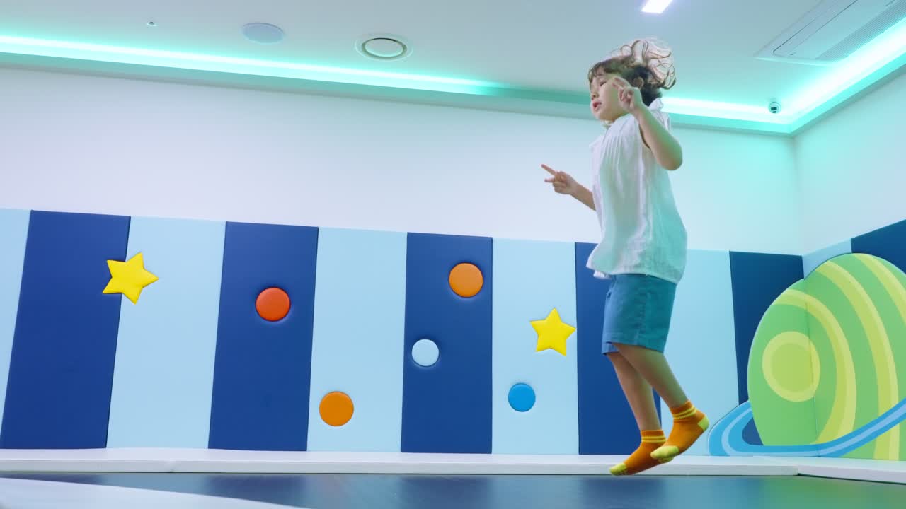 Toddler having fun jumping on trampoline at colorful indoor playground, having fun and making faces