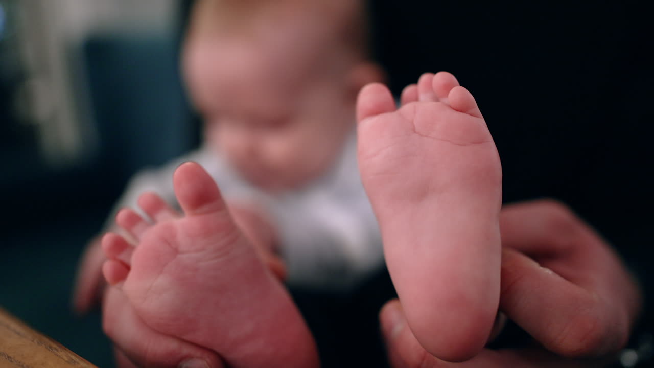 Father's hands hold the tiny bare feet of his son. Little baby boy in dad's arms. Close up.