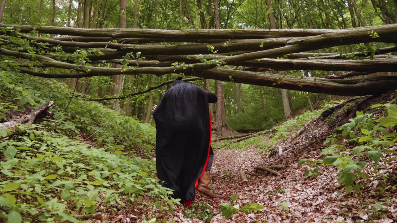 vista posterior de un ángel de la muerte con capa negra encapuchada bailando en el bosque