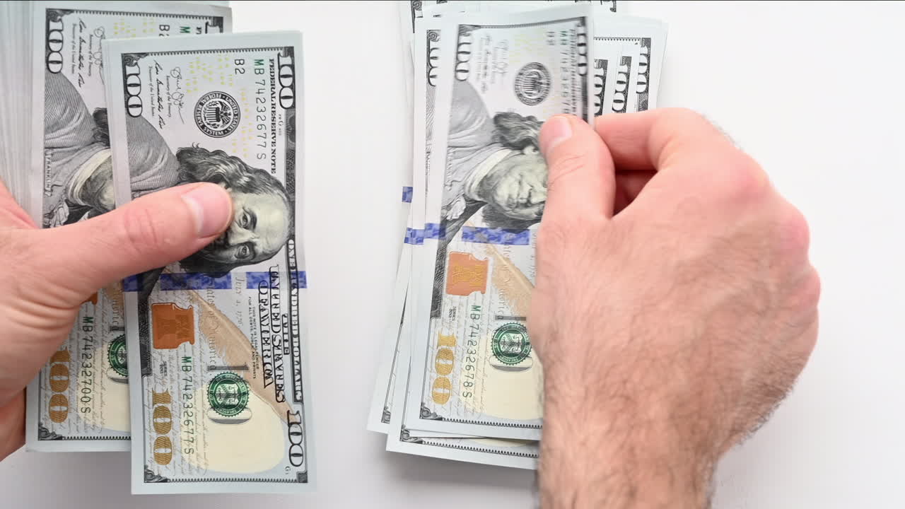 A man's hands quickly count a stack of one hundred dollar bills against a light background
