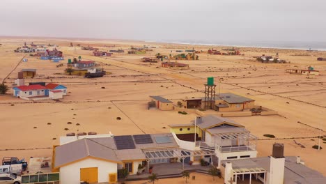 Antenne-über-Einer-Seltsamen,-Einsamen,-Kargen-Postapokalyptischen-Strandsiedlung-Von-Sommerhäusern-In-Hengtiesbaai-Namibia-1