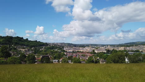 left to right pan shot of the city of bath skyline from hillside lookout on a sunny summer’s day with blue sky - white fluffy clouds