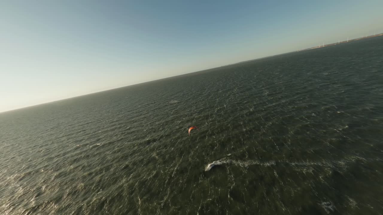 Aerial flight above lone wind kite surfer in rough ocean waves
