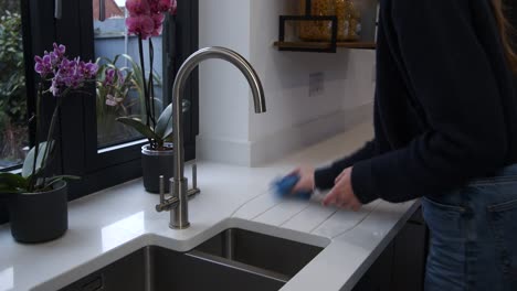 female model wiping down a white quartz worktop by a sink in a kitchen