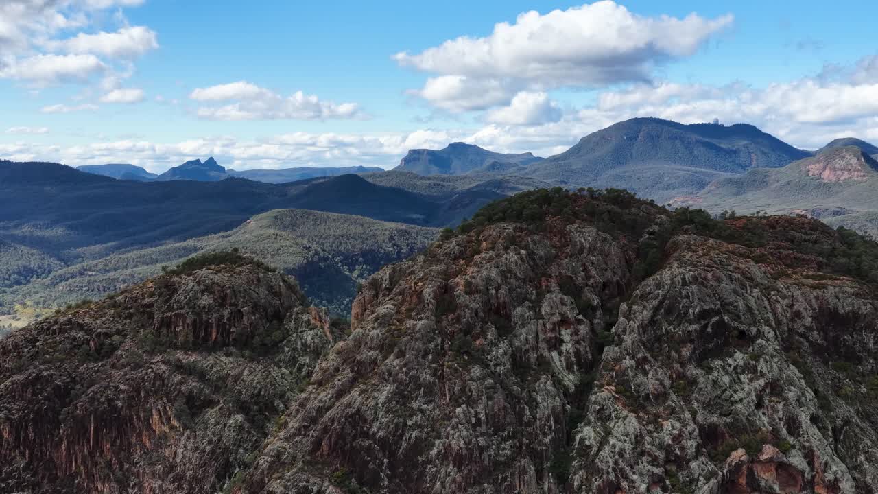Camera slowly pans across rugged rock formations and distant mountain ranges under partly cloudy skies in Warrumbungle National Park, with natural daylight and wide landscape perspective