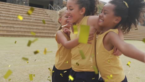animation of gold confetti over happy diverse schoolgirls celebrating and hugging on sports field