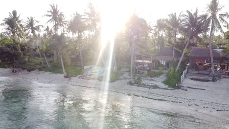 People-at-ShakaBrah-Beachfront-Café-and-Bungalows-on-Siargao-island-with-tropical-sand-beach-and-sunset-sun-flare-through-palm-trees