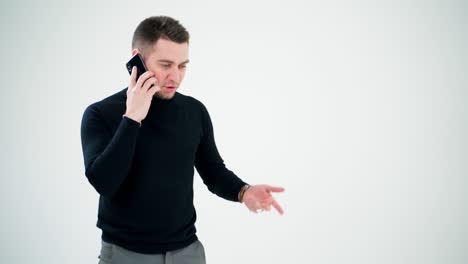 Businessman leading e business through the phone. Young man in black sweater and grey trousers talking on the mobile phone on white background.