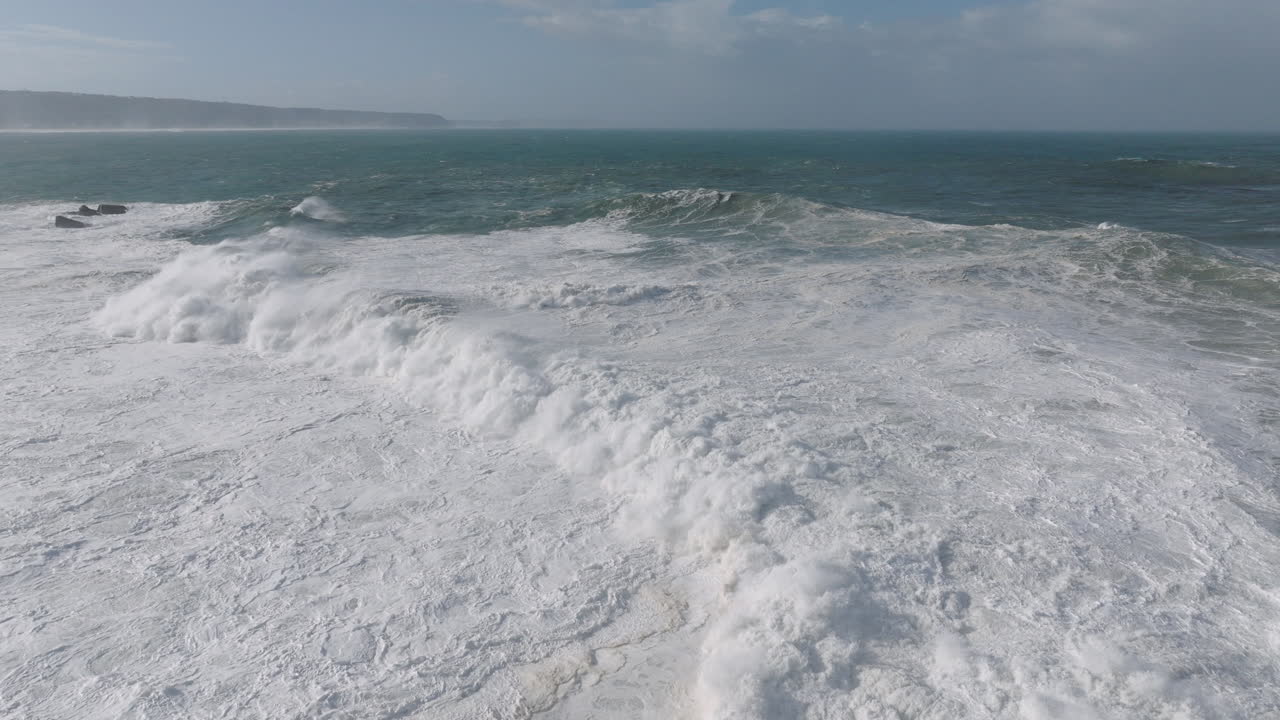 Aerial drone shot of big waves coming into shore on a day with giant waves in Nazaré, Portugal, Europe. View from beach. Nazare, town with biggest recorded waves in the world
