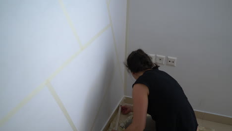 mujer caucásica aplicando cinta de papel en la pared, preparándose para pintar en interiores