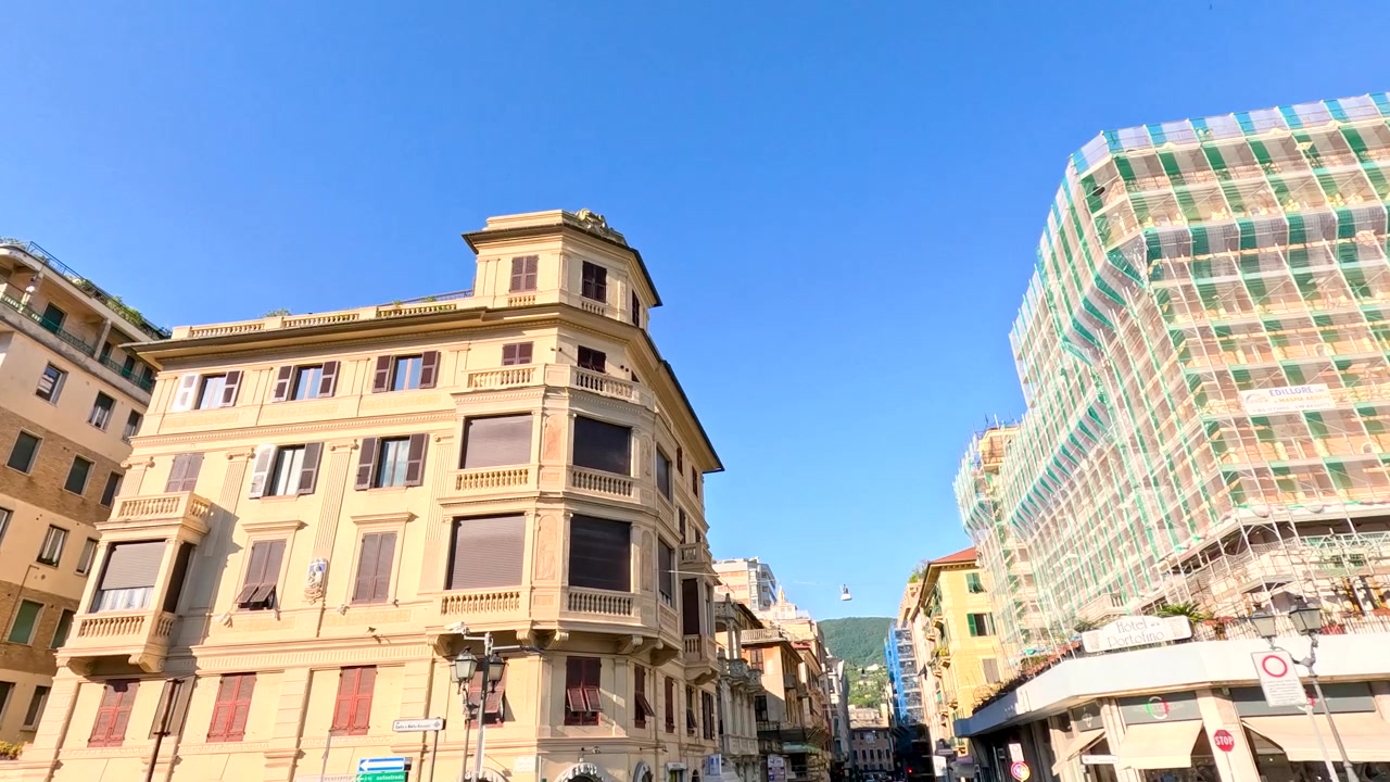 Una telecamera ad angolo basso effettua una panoramica su edifici storici e colorati sotto un cielo azzurro e limpido.