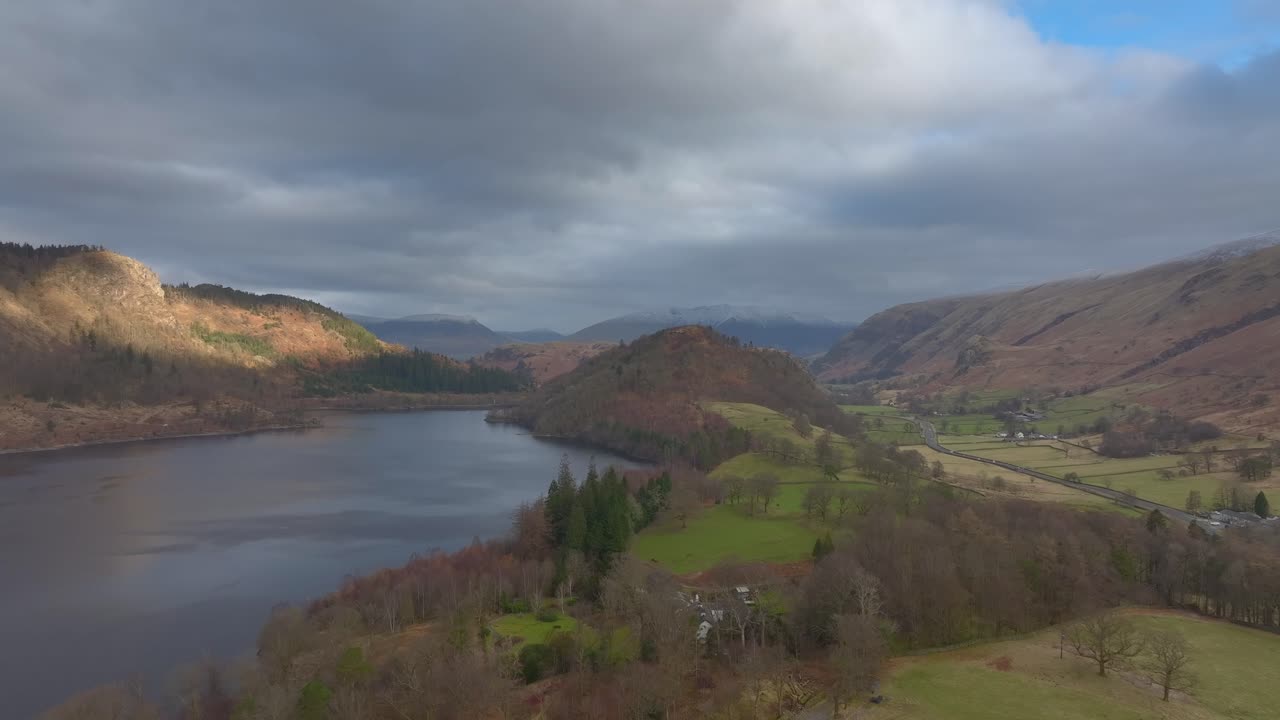 Flying down wide valley with lakeside road and dark lake in winter. Lake District, Cumbria, UK.