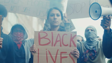 portrait of a caucasian woman holding a black lives matter" signboard in a protest with multiethnic group of people in the street"