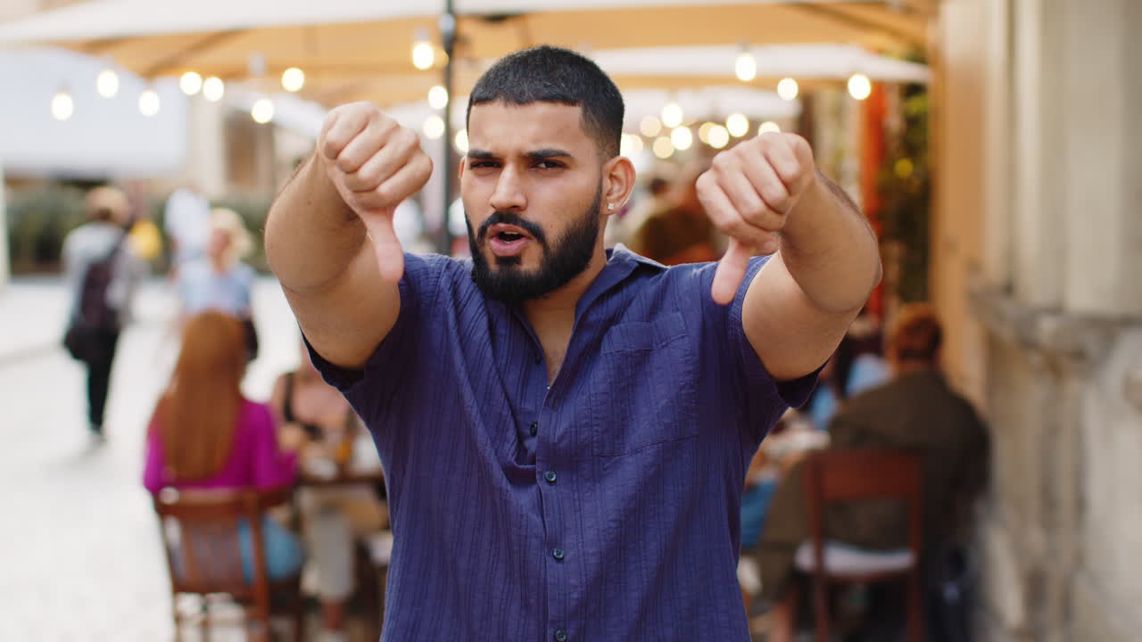 Upset young man guy showing thumbs down sign disapproval dissatisfied bad work mistake in city