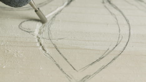 woodworker using electric engraving tool to make carved decoration on piece of wood, close-up