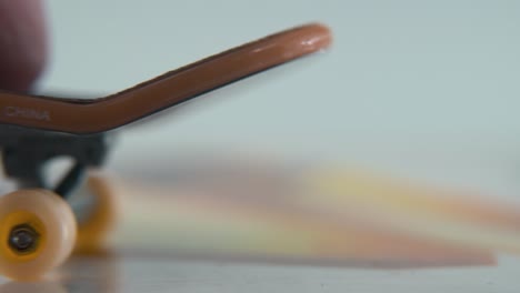 una toma hiper macro detallada de un mini patineta, pequeñas ruedas blancas, montar fingerboard de izquierda a derecha, hacia atrás y hacia adelante, iluminación profesional, vídeo estático cinematográfico 4k
