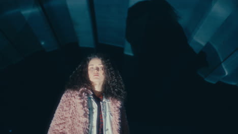portrait of young woman in stylish fur coat under city bridge at night