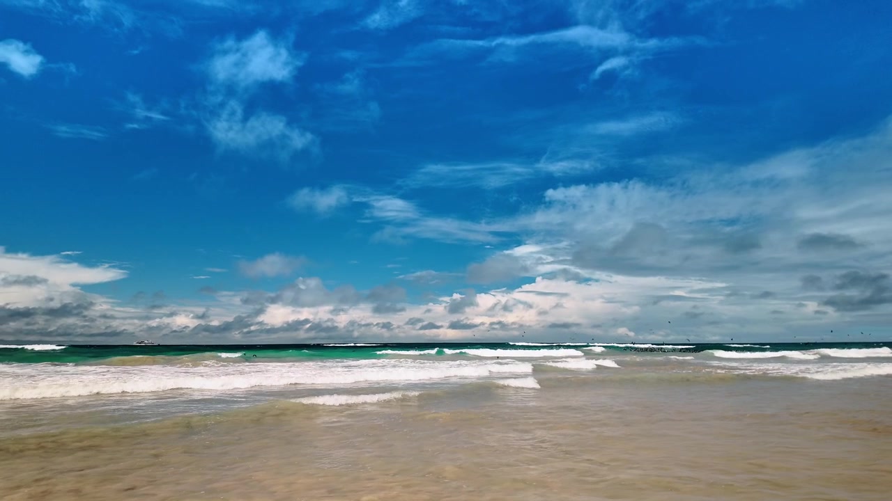 Ampia vista di una spiaggia sabbiosa con onde turchesi dell'oceano. Vista panoramica di una costa sabbiosa con onde che si infrangono sotto un cielo azzurro brillante sull'isola Isabela, Galapagos