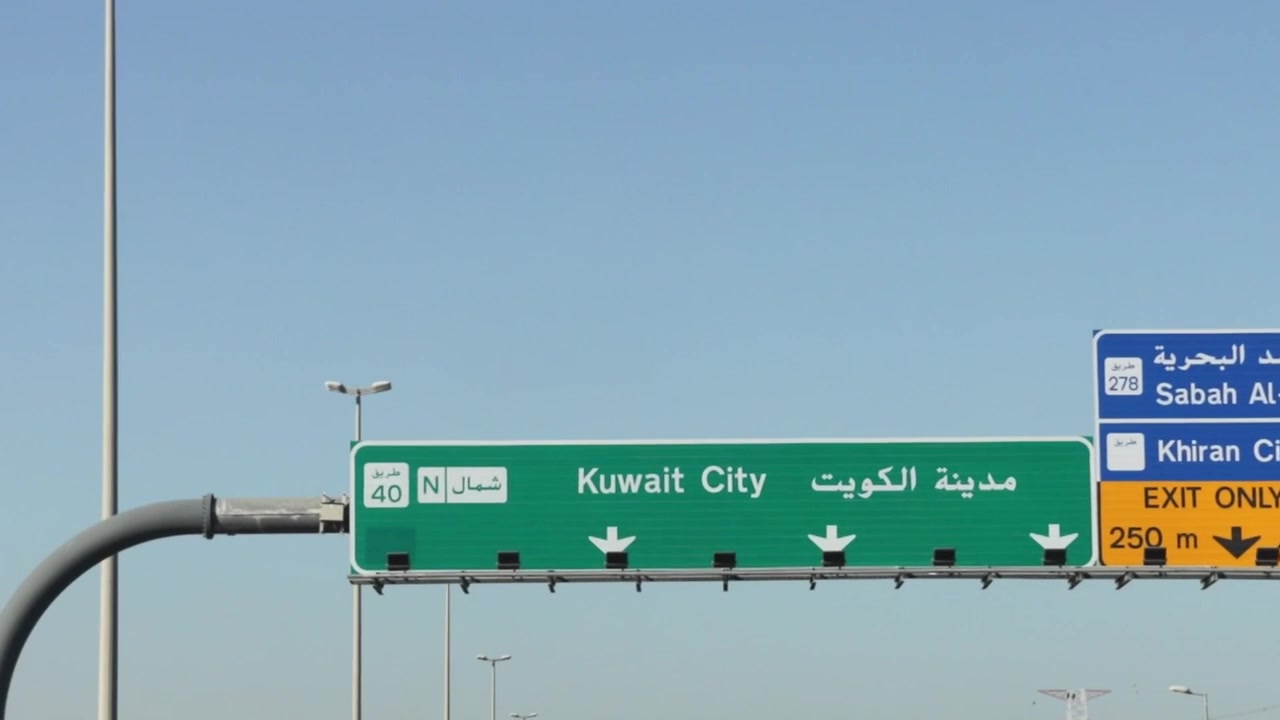 Drogowy znak autostradowy wskazujący kierunek do Kuwejtu w języku angielskim i arabskim