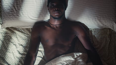 young black bare-chested man with open eyes in bed, overhead pull-out